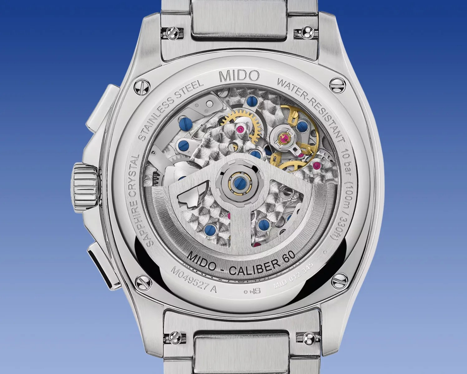 Back view of a stainless steel Mido wristwatch showcasing the intricate Mido Caliber 60 automatic movement through a sapphire crystal case back. The watch is water-resistant up to 10 bar (100 meters/330 feet) and features visible gears, screws, and jewels in silver, gold, blue, and pink tones. The bracelet is also stainless steel with a brushed finish.
