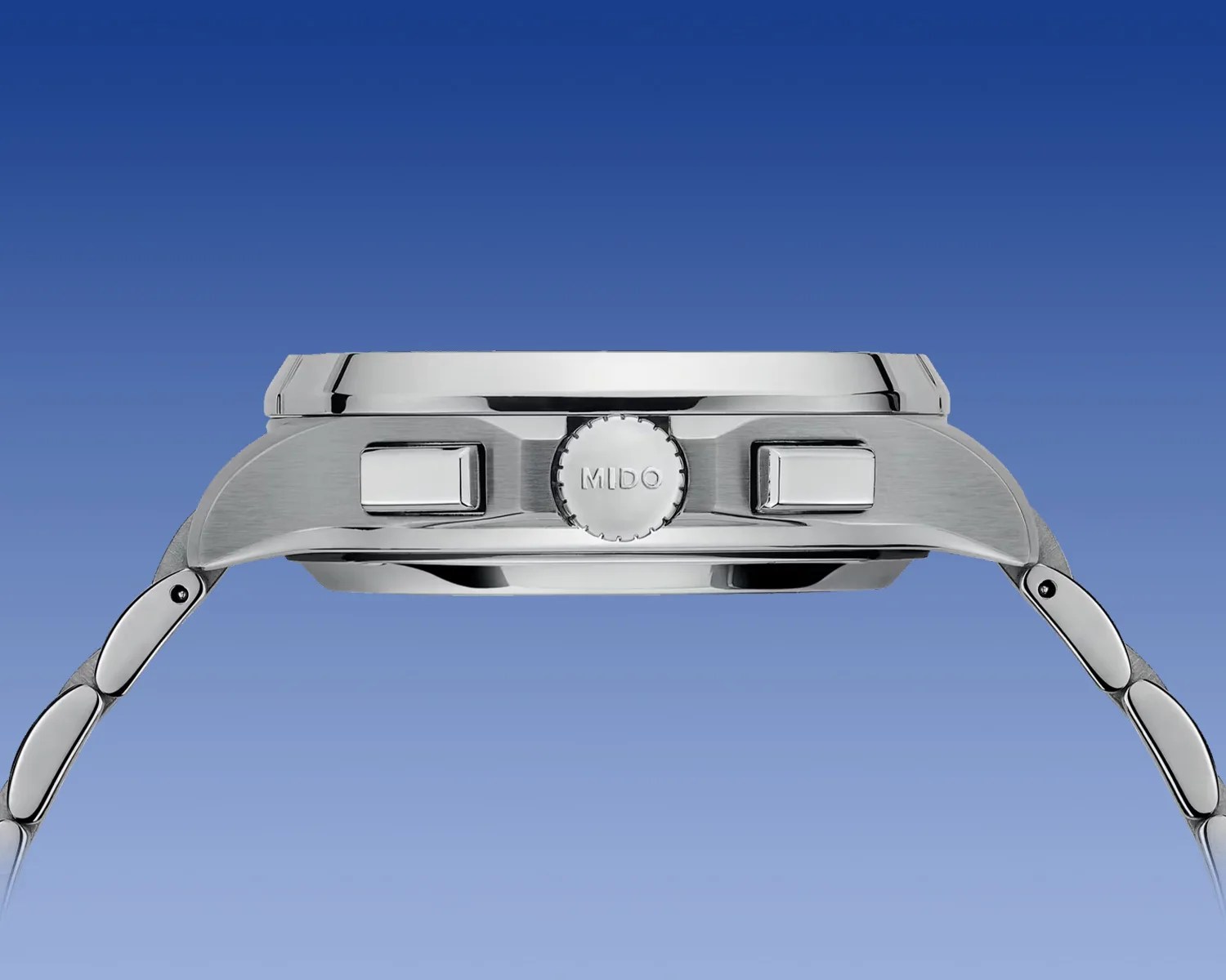 Side view of a silver stainless steel wristwatch with a polished case, featuring two rectangular push buttons and a ridged crown engraved with the brand name "MIDO." The watch is attached to a matching metal link bracelet. The background is a gradient blue.