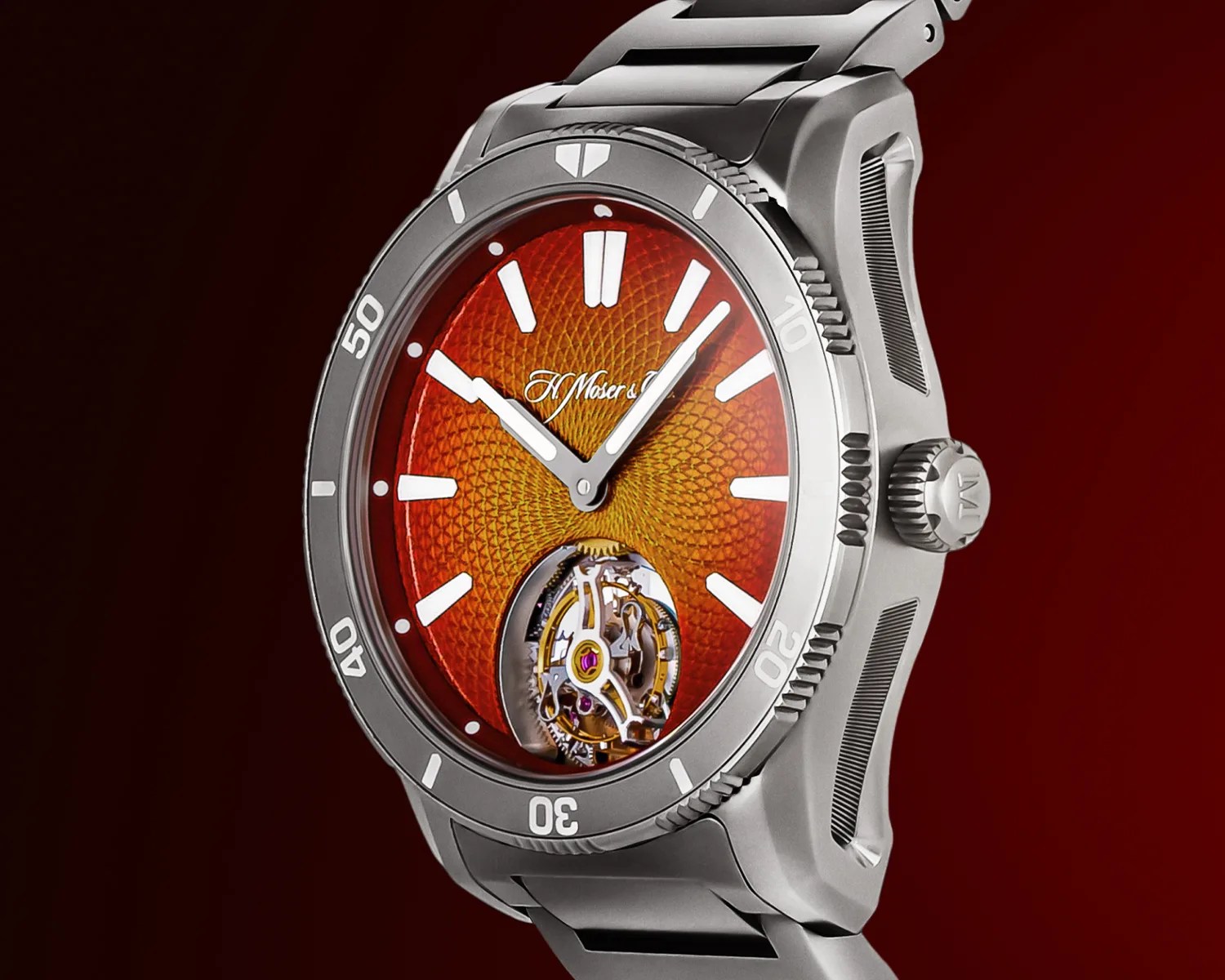 Silver moser wristwatch with a textured orange dial featuring white hour markers and hands. The watch has a visible tourbillon mechanism at the 6 o'clock position and a rotating bezel with minute markers. The crown is engraved with the brand's initials. The watch is set against a dark red background.