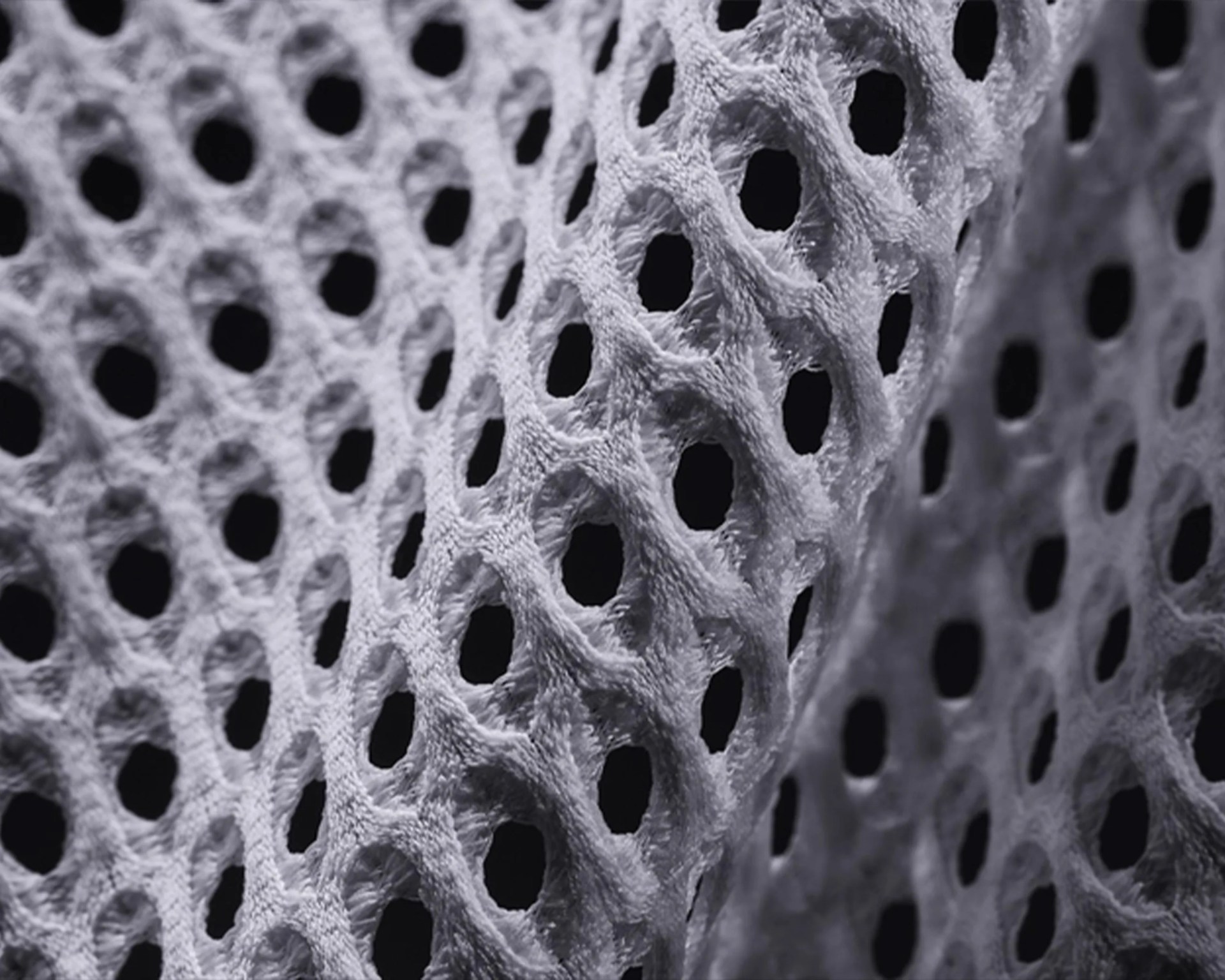 Close-up of a textured, white mesh fabric with a pattern of evenly spaced oval holes, showing the detailed fibers and soft, slightly fuzzy surface.