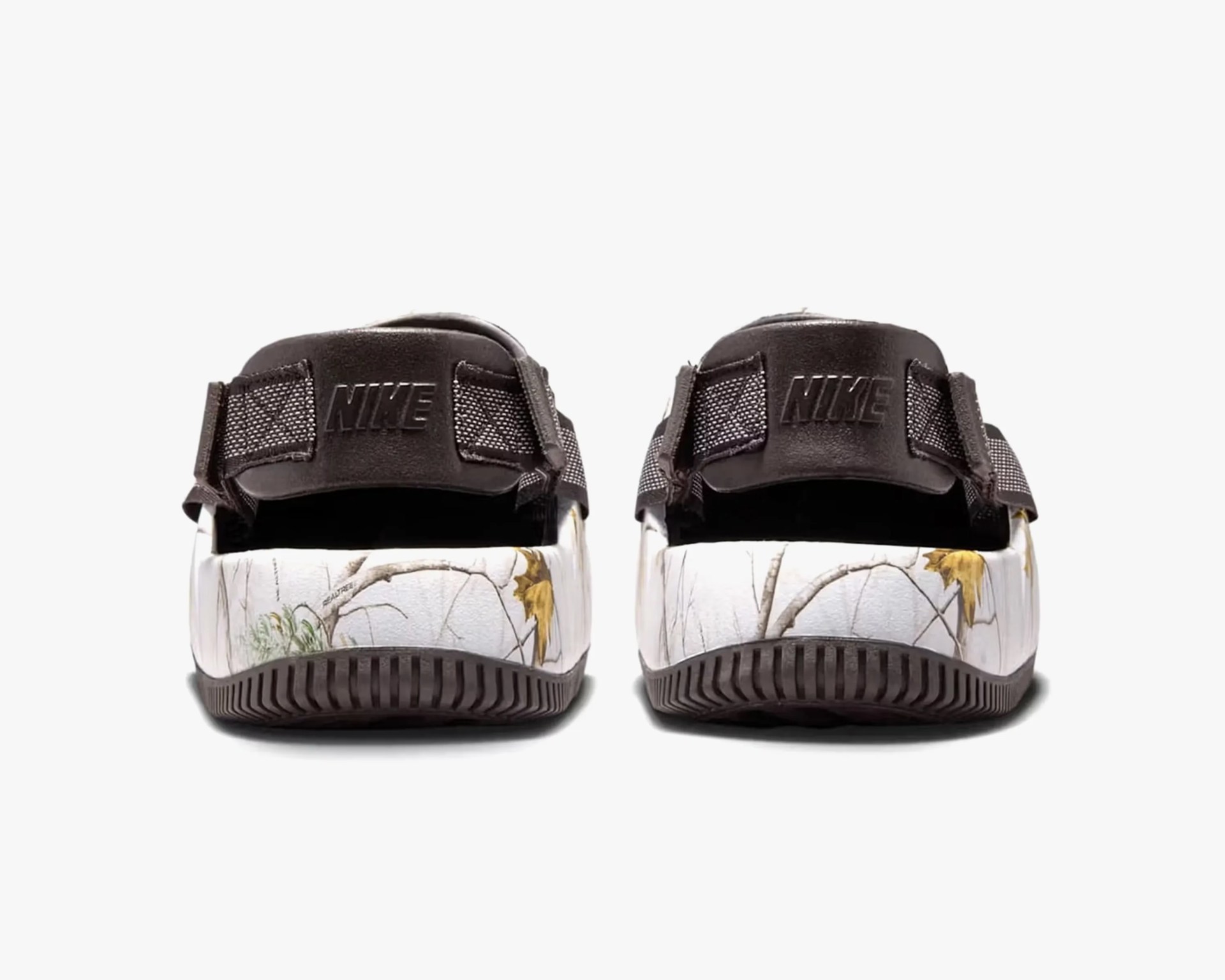 Pair of Nike sandals shown from the back, featuring black straps with the Nike logo embossed on the heel strap. The midsole has a white base with a nature-inspired print of branches and leaves in muted colors. The outsole is black with a textured pattern for grip.