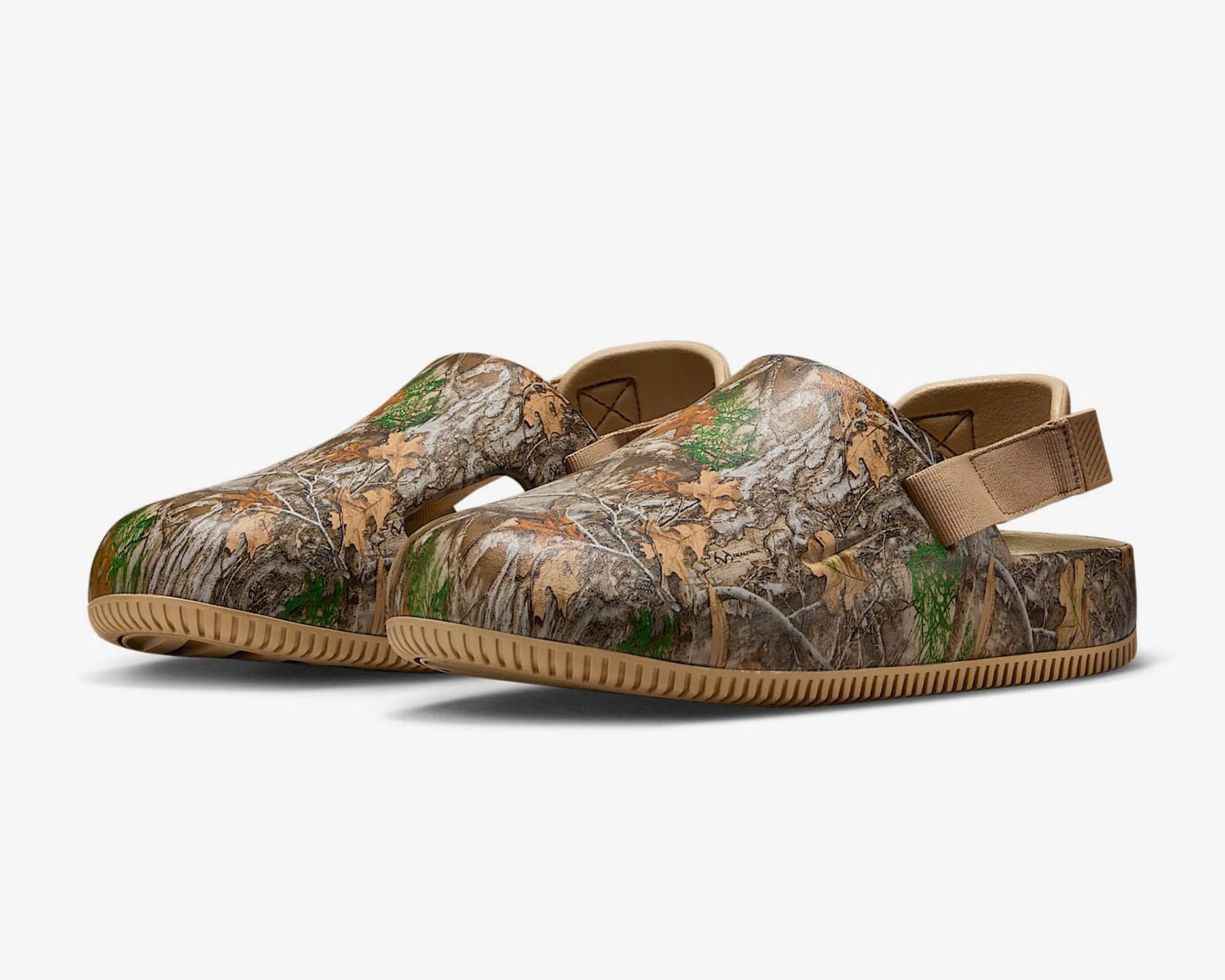 Pair of slip-on clogs with a camouflage pattern featuring brown, tan, and green leaves and branches, tan adjustable heel straps, and tan textured soles.
