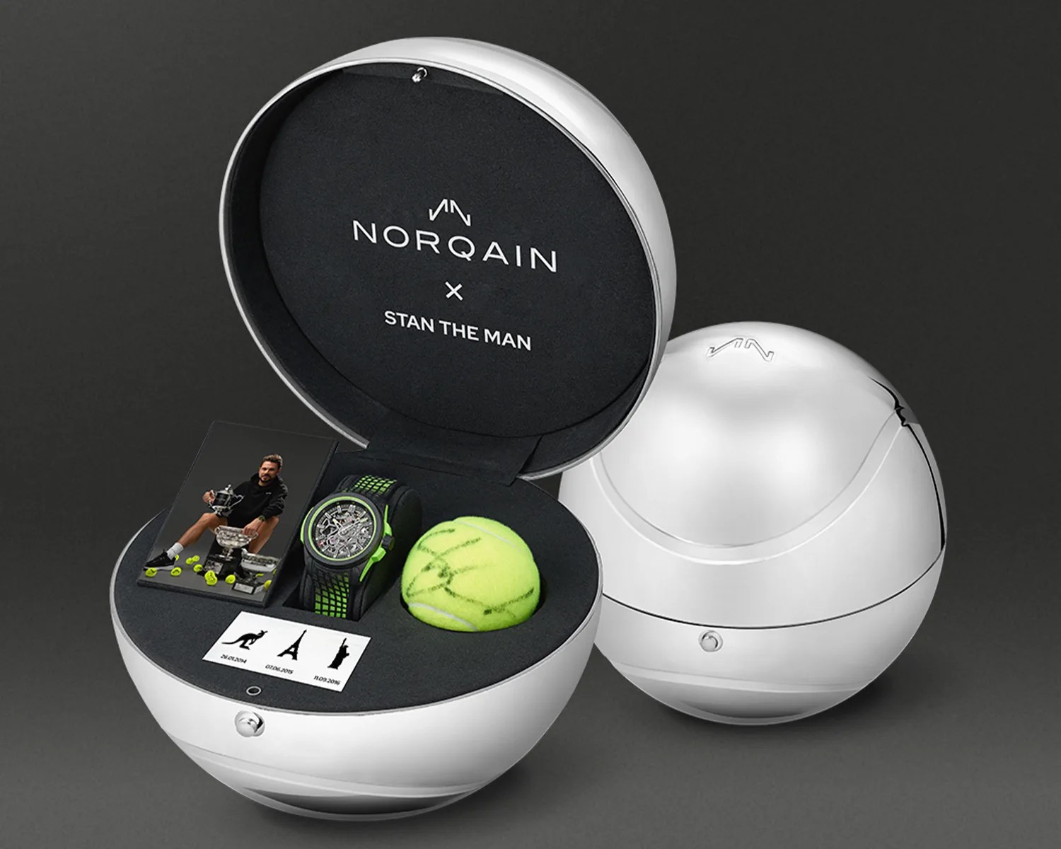 A spherical silver watch box with a black interior, branded with "NORQAIN x STAN THE MAN." Inside the box is a green and black wristwatch, a tennis ball with green markings, a small photo of a man holding trophies surrounded by tennis balls, and a card with three icons and dates. Another closed spherical box is placed beside it.
