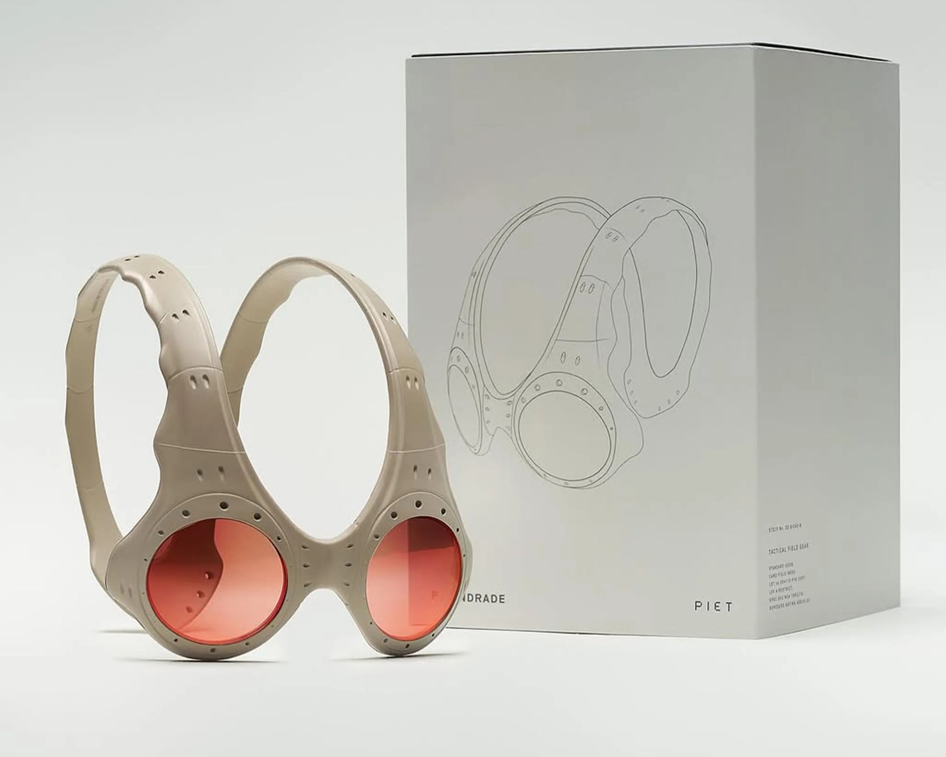 Beige protective eyewear with round, red-tinted lenses and a double-strap design, displayed next to its matching beige box featuring a line drawing of the eyewear on the front.