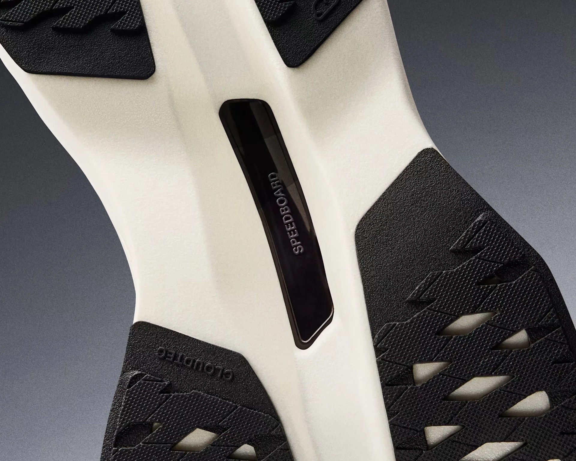 Close-up of the sole of a shoe featuring a white midsole with black textured rubber sections. The black section on the left side has the word "CLOUDTEC" embossed, and the central black insert has the word "SPEEDBOARD" printed on it. The sole design includes cut-out patterns in the black rubber areas.