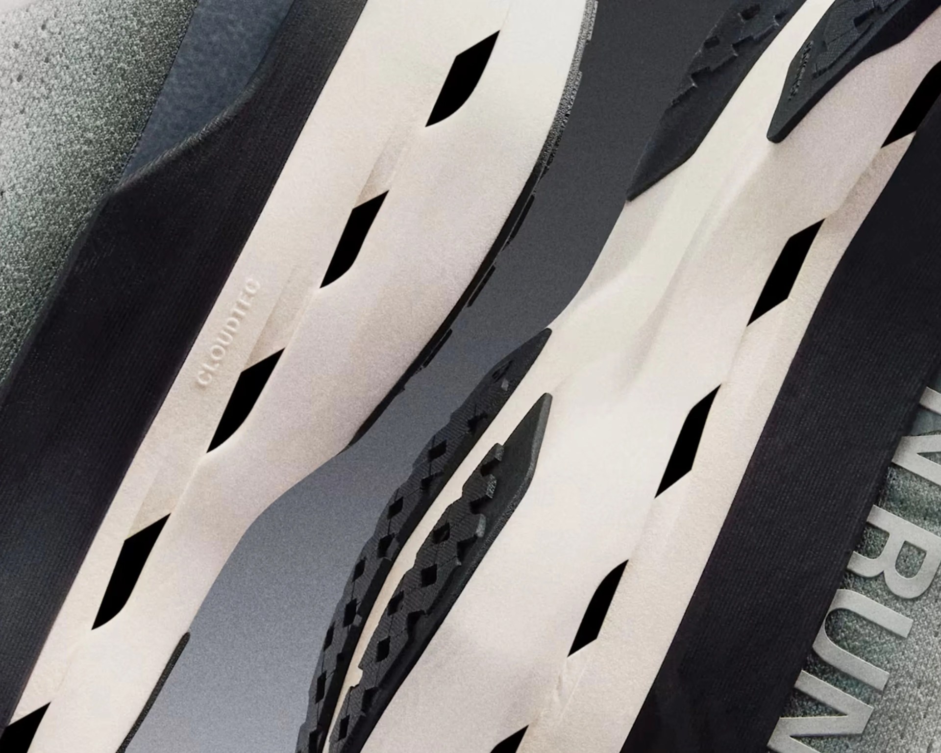 Close-up of the sole of a shoe featuring a white midsole with black diamond-shaped cutouts and black rubber tread. The word "CLOUDTRO" is embossed on the white midsole. The background includes a textured gray surface with partially visible text.