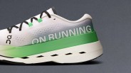 White and green running shoe with black laces, featuring the text "ON RUNNING" on the side and a gradient design from white to green on the midsole. The shoe has a perforated upper and a thick, cushioned sole with cut-out details.