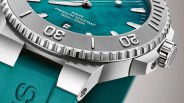 Close-up of a stainless steel dive watch with a teal dial and matching teal rubber strap.