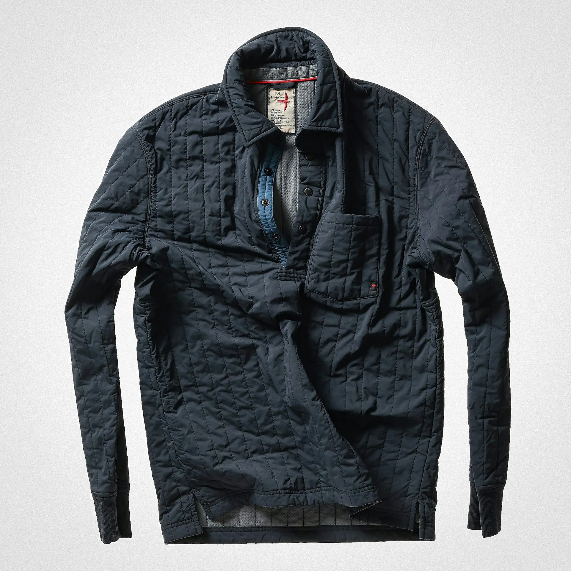 Quilted long-sleeve pullover shirt in dark navy with a stand collar, partial button placket, and a chest pocket. The shirt features vertical quilting and ribbed cuffs. The inner placket has a contrasting blue fabric.