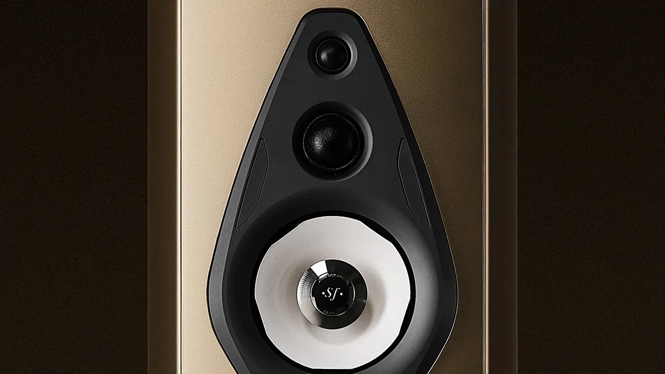 Close-up of a high-end speaker driver assembly featuring a gold-colored cabinet. The speaker has three drivers arranged vertically: a small tweeter at the top, a midrange driver below it, and a larger woofer at the bottom with a distinctive white cone and a central black dome marked with "sf." The drivers are mounted on a black, teardrop-shaped baffle.