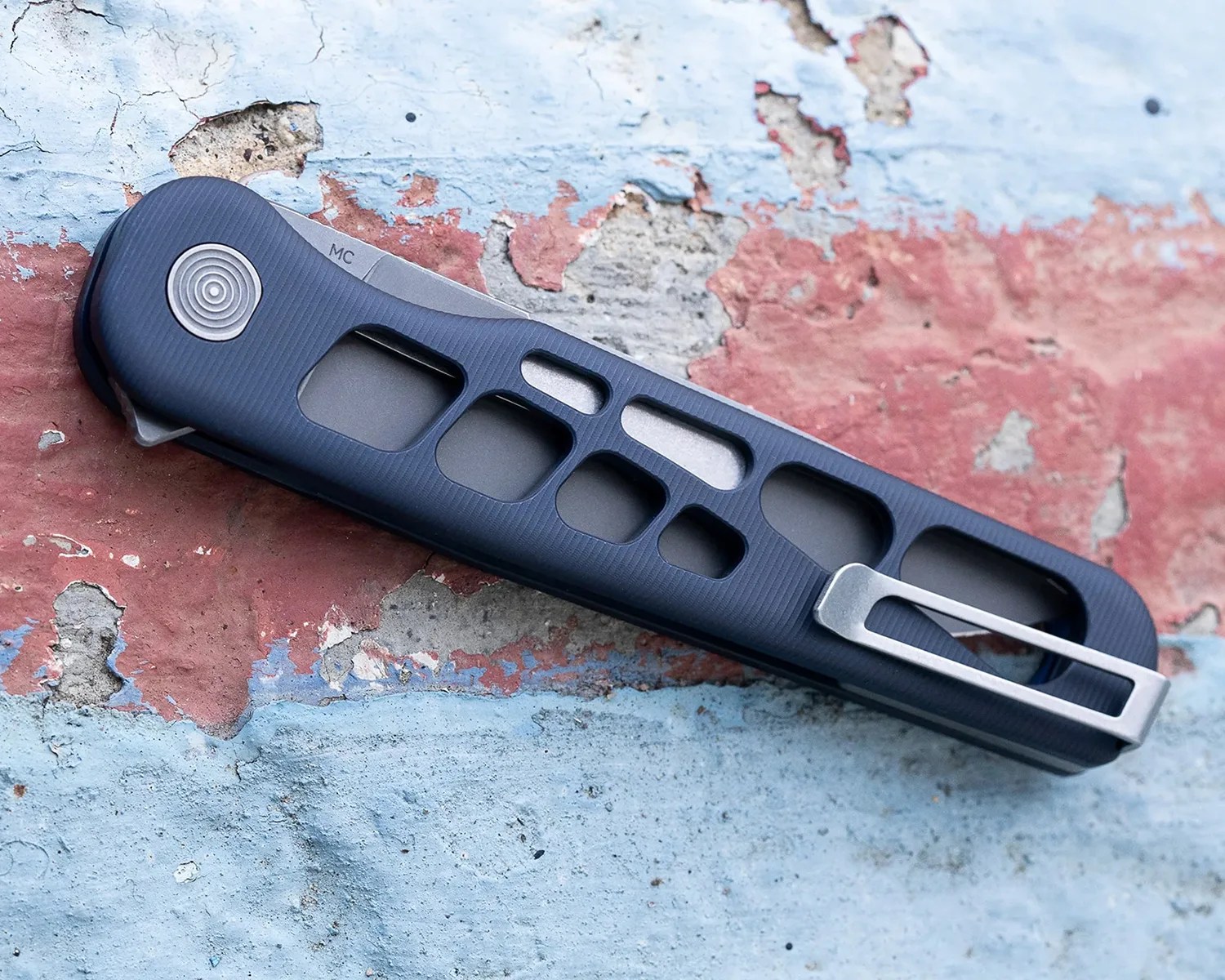 Folded pocket knife with a dark blue handle featuring multiple cut-out sections and a silver clip, resting on a weathered surface with peeling red and blue paint.