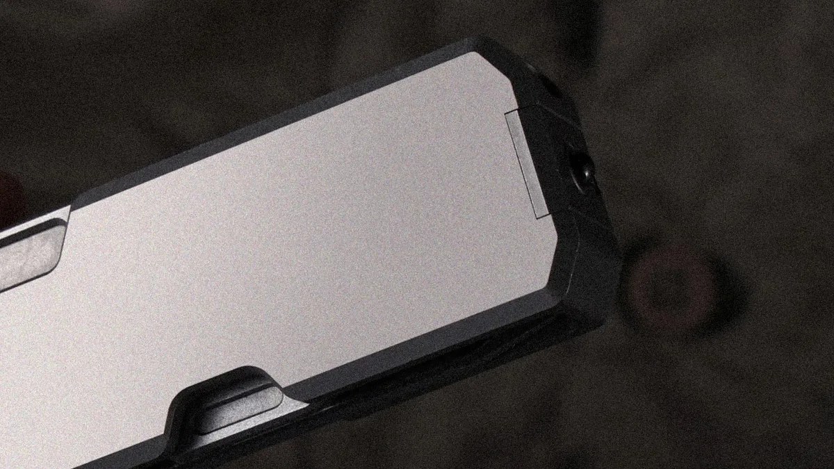 Close-up of the slide of a semi-automatic handgun, showing the rear portion with a metallic finish and black accents. The background is blurred and dark.
