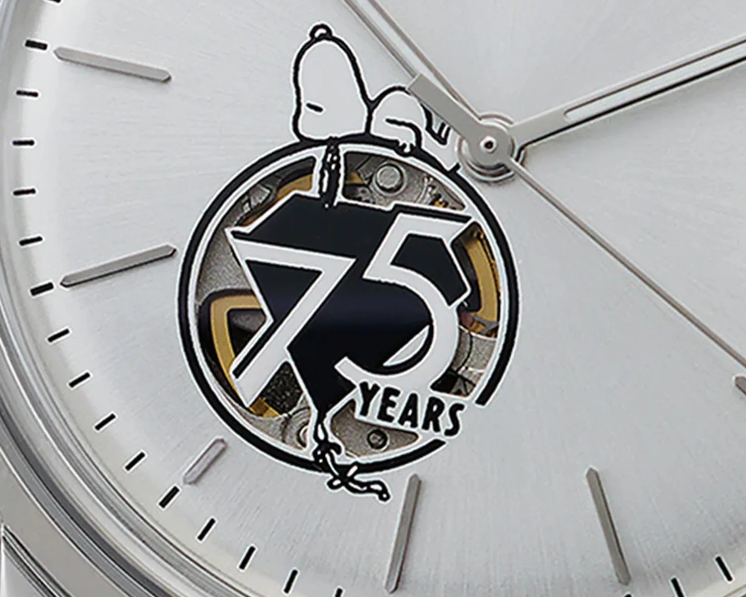 Close-up of a Timex watch face featuring a "75 YEARS" emblem with Snoopy lying on top of the number 75, integrated into the watch's open mechanism. The watch has a silver background with simple hour markers and silver hands.