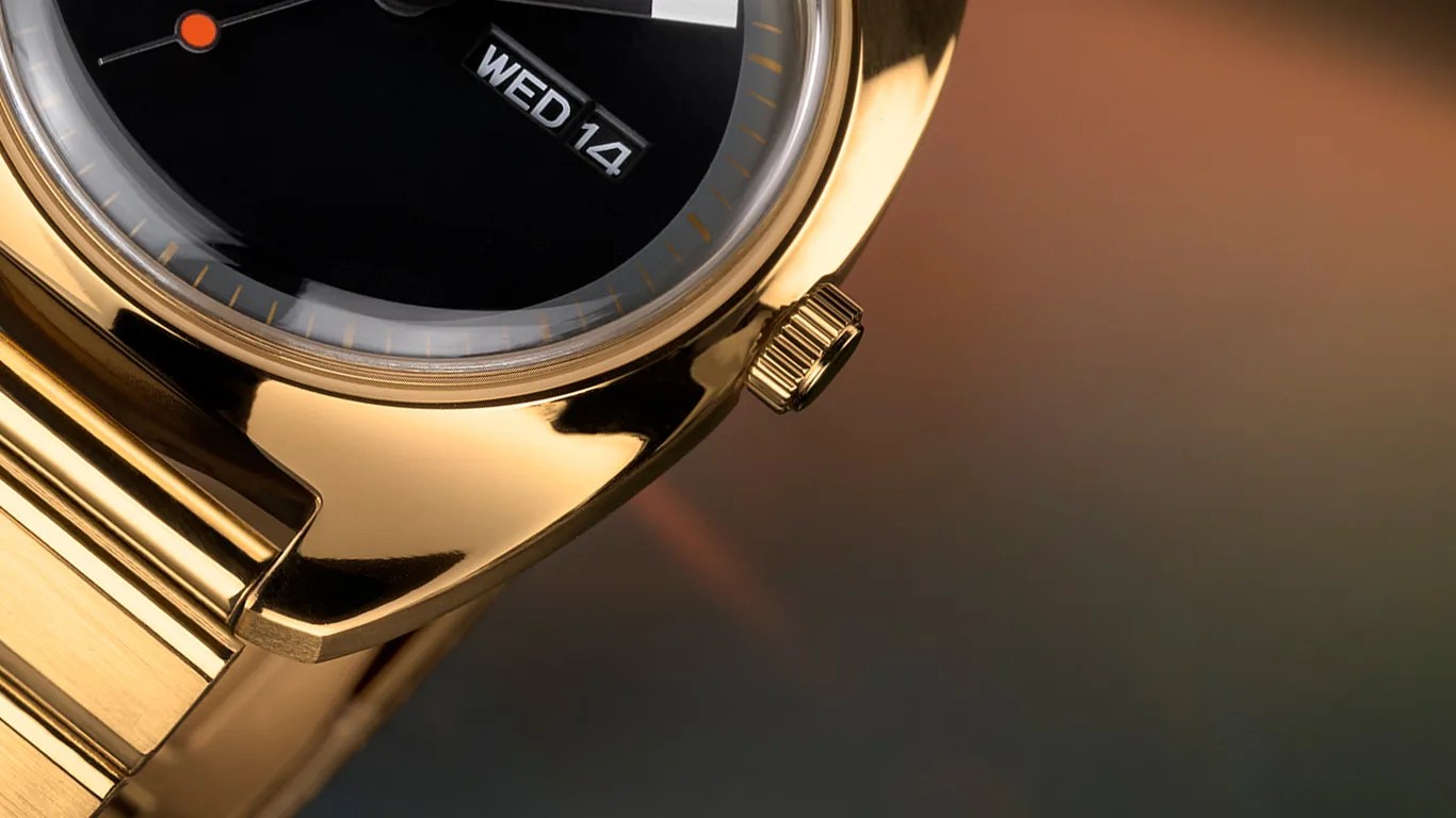 Close-up of a gold Timex wristwatch showing part of the black dial with a day and date display reading "WED 14," a gold crown, and a portion of the gold bracelet.