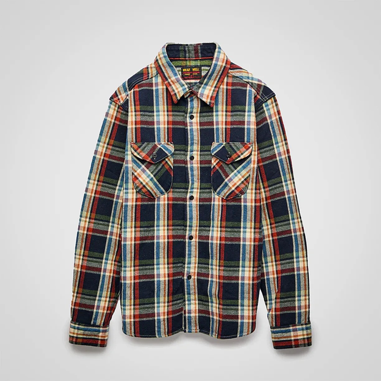 Long-sleeve button-up flannel shirt with a multicolored plaid pattern featuring navy blue, red, green, cream, and light blue. It has a classic collar and two chest pockets with buttoned flaps.