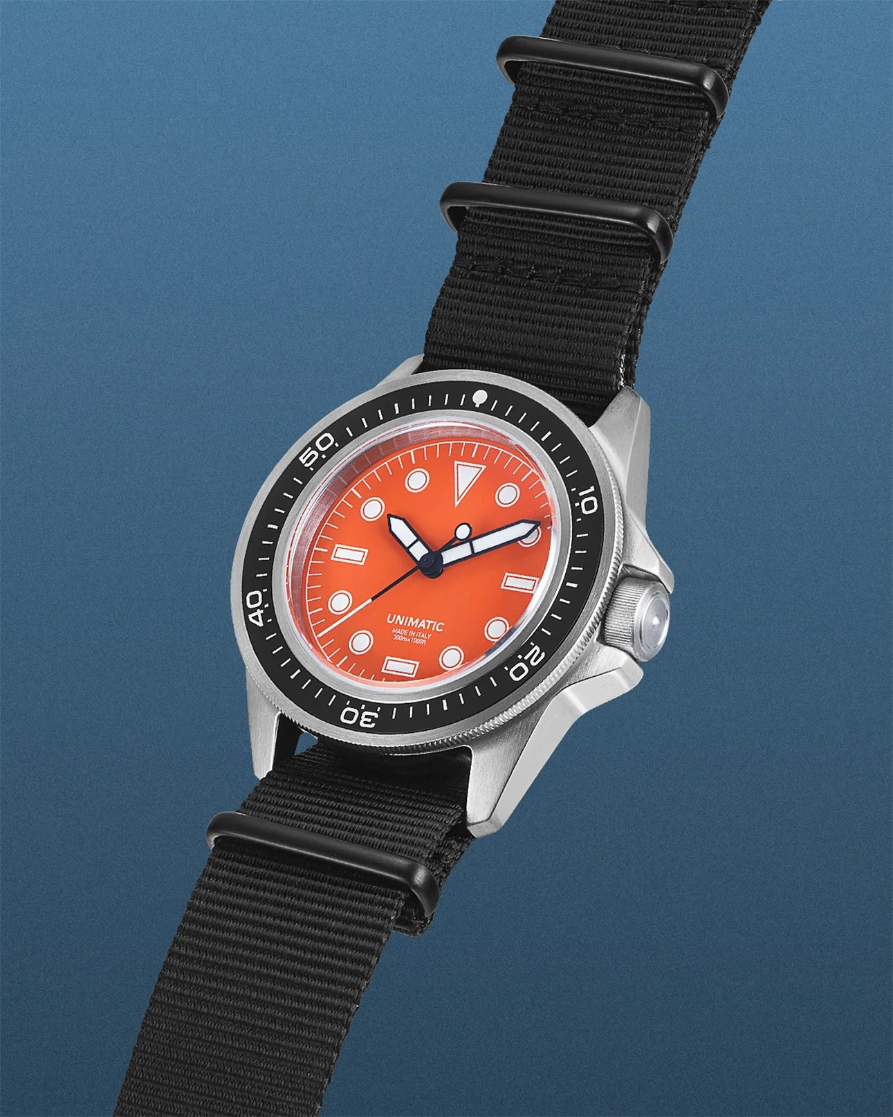 Stainless steel wristwatch with a bright orange dial, black bezel marked with white numerals, and a black nylon strap. The dial features white geometric hour markers and bold black and white hands. The brand name "UNIMATIC" and "MADE IN ITALY 300m=1000ft" are printed near the 6 o'clock position.