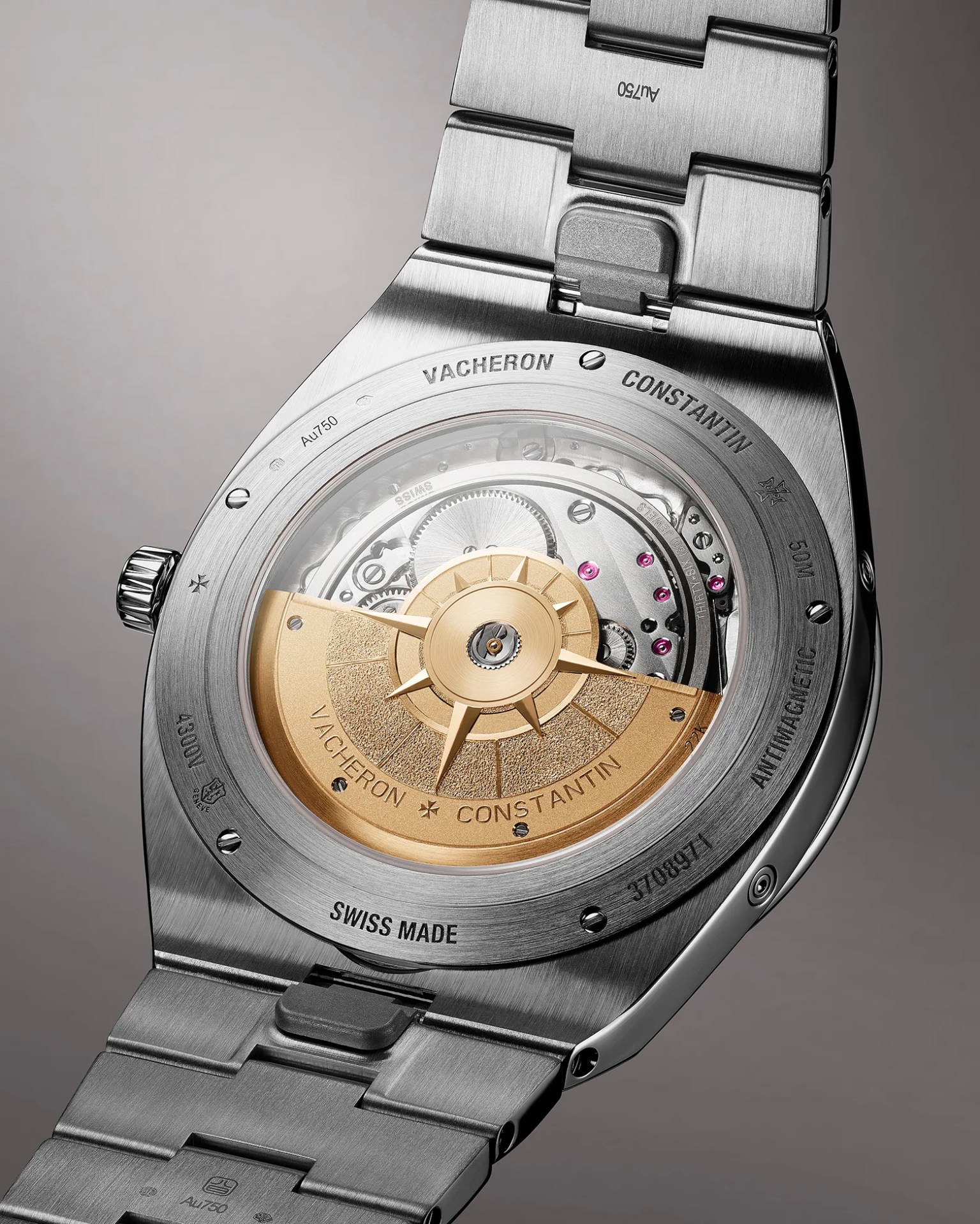 Back view of a Vacheron Constantin wristwatch showcasing its automatic movement through a transparent case back. The watch features a stainless steel bracelet and case, with visible engravings including "VACHERON CONSTANTIN," "SWISS MADE," "ANTIMAGNETIC," "50M," and "4300U." The rotor is gold-toned with the brand name engraved on it, and the intricate mechanical components inside are visible, including gears and jewel bearings.