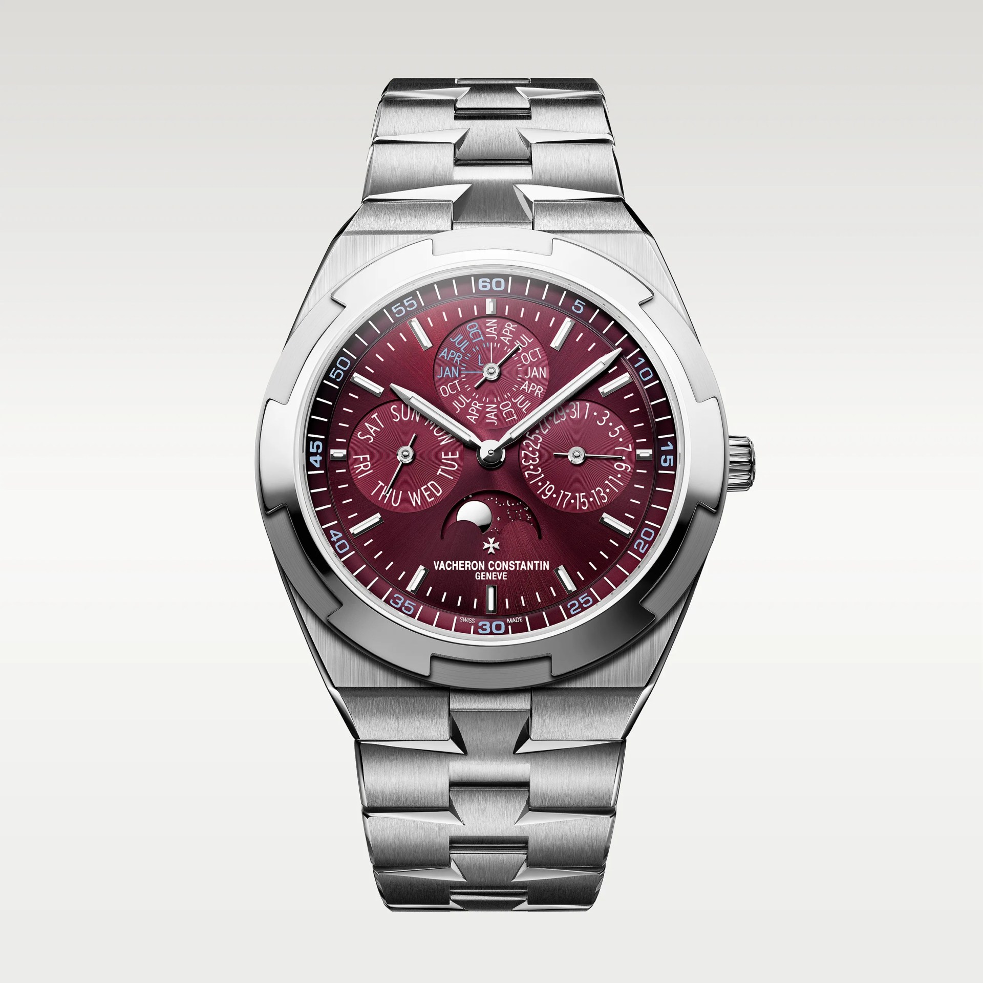 Silver stainless steel wristwatch with a burgundy dial featuring three subdials displaying the day, date, and month, along with a moon phase indicator at the 6 o'clock position. The watch has silver hour markers and hands, a notched bezel, and a linked bracelet. The brand name "Vacheron Constantin Gen&egrave;ve" is printed above the 6 o'clock position.