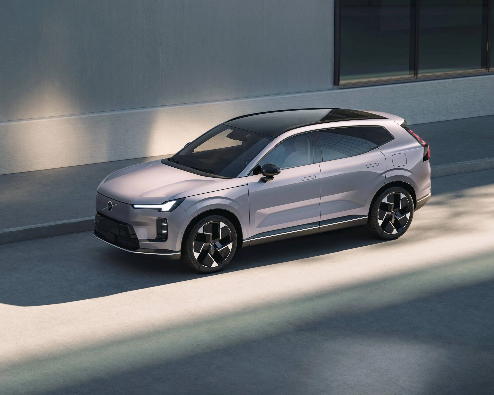 Silver compact SUV with a sleek, modern design featuring a black roof, black side mirrors, and distinctive black and silver alloy wheels, parked on a concrete surface next to a minimalist building with large windows.