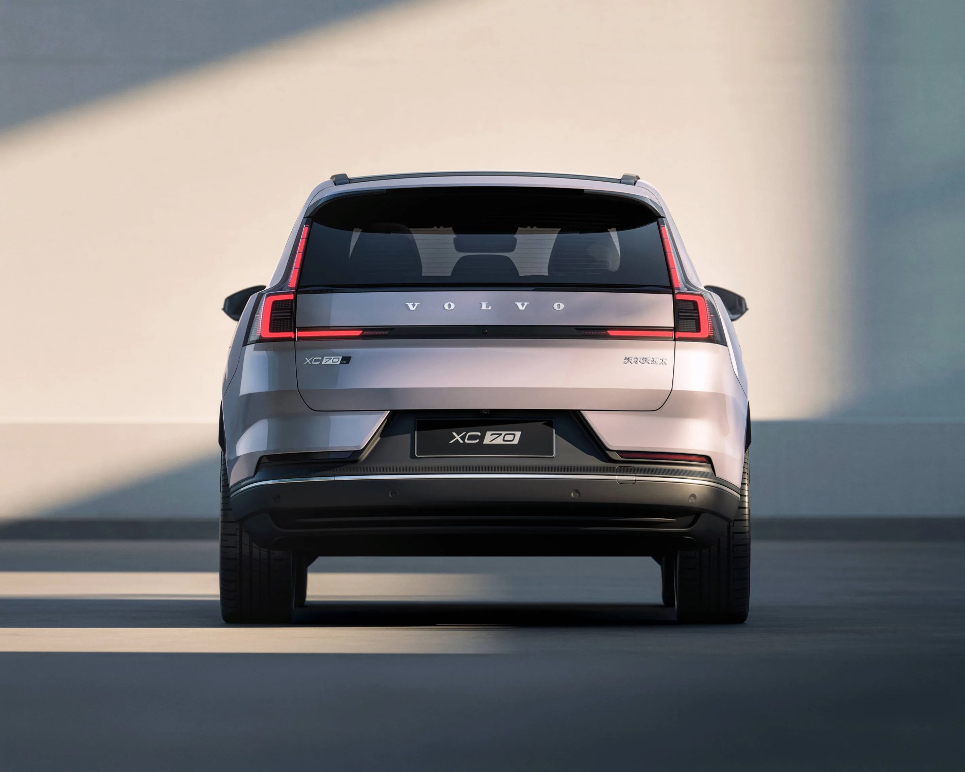 Rear view of a silver Volvo XC70 SUV with distinctive vertical and horizontal LED tail lights, a black lower bumper, and the Volvo logo prominently displayed across the rear window area. The license plate area reads "XC70.