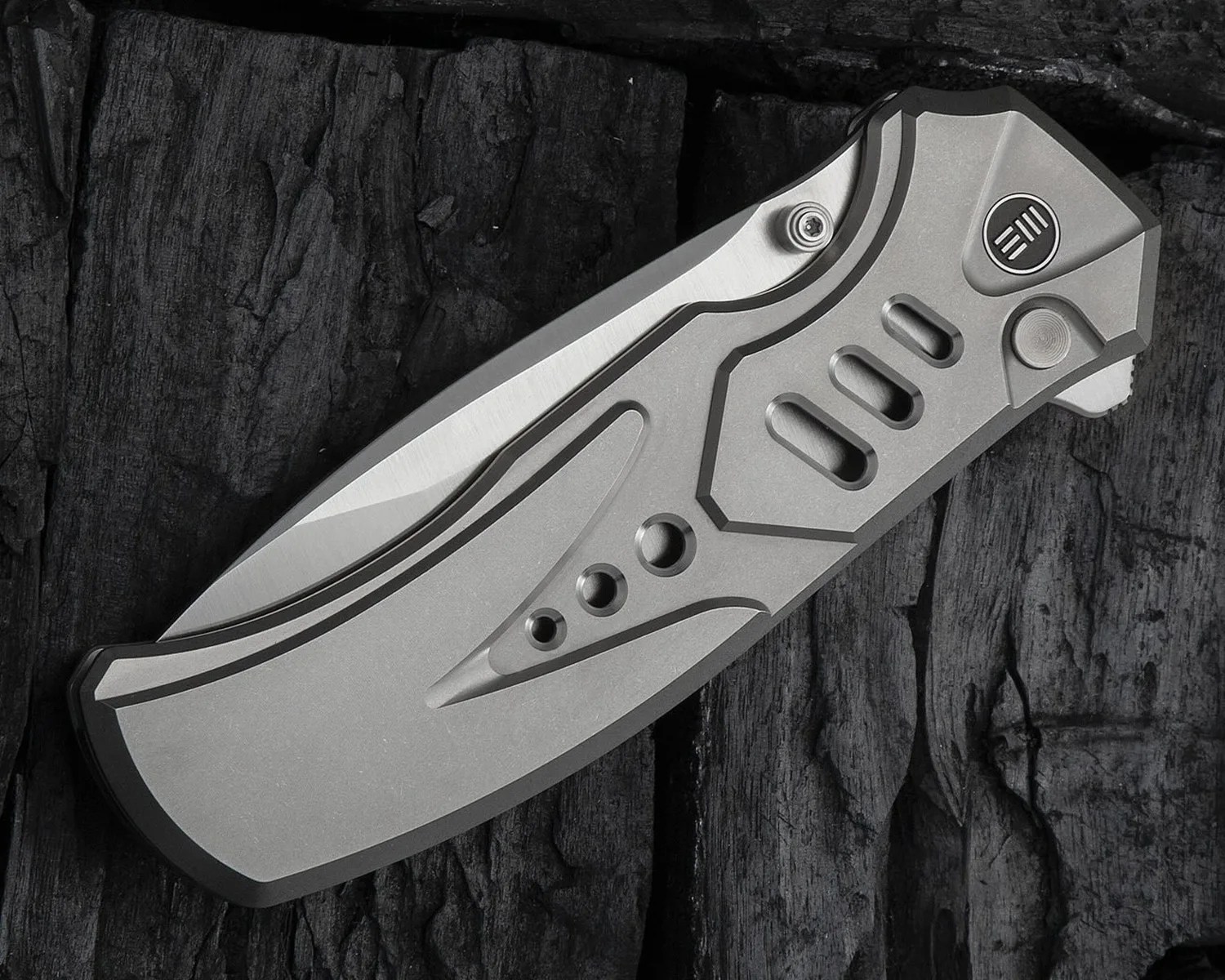 Folded metallic pocket knife with a sleek, modern design featuring multiple cutouts and grooves on the handle, resting on a textured dark wooden surface.