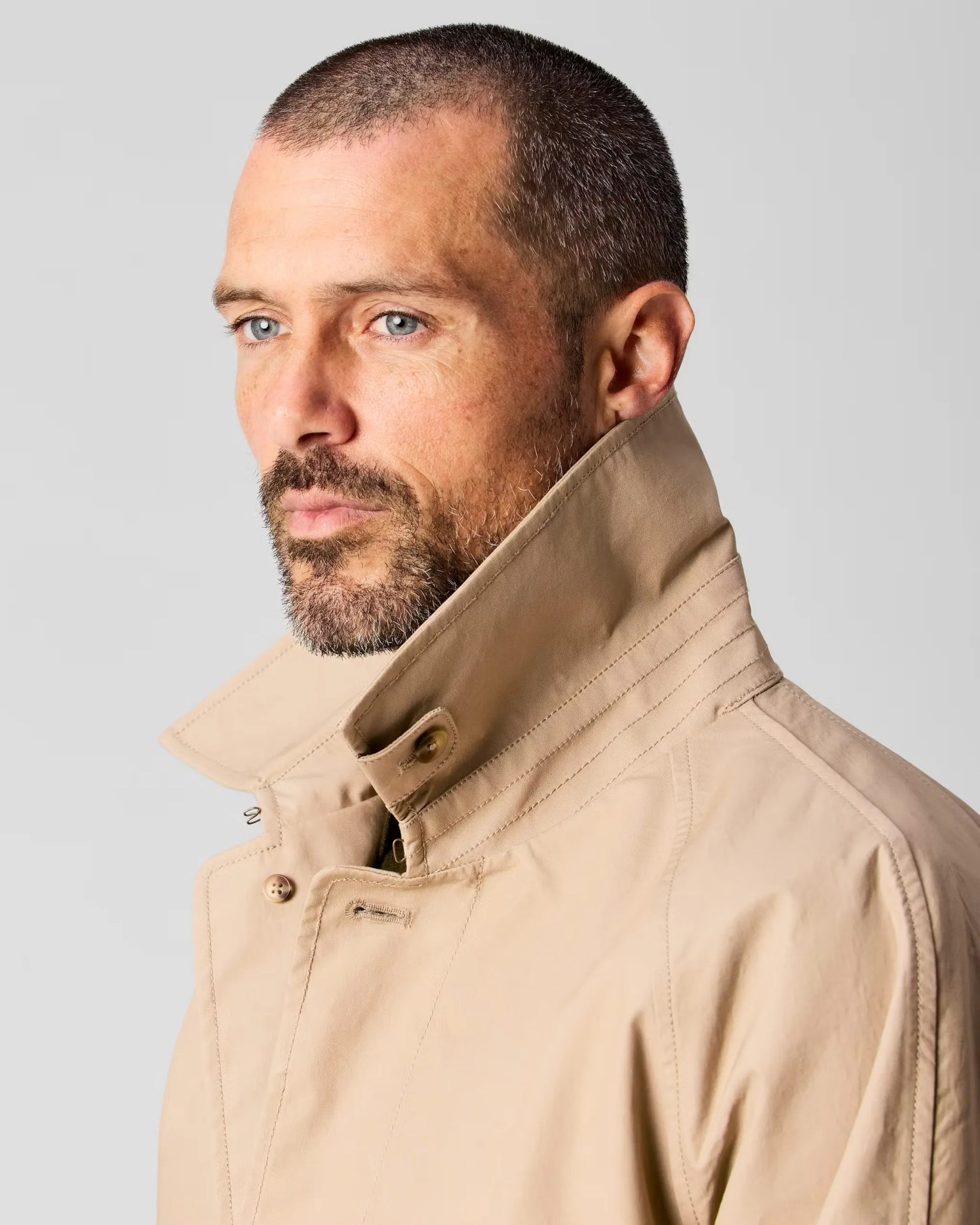 the profile view of a man in a khaki Wills trench coat