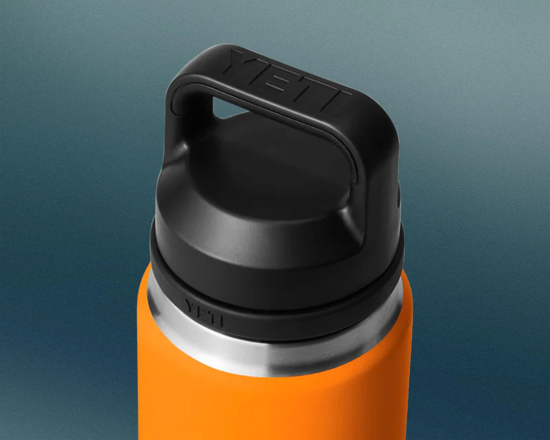 Close-up of the top portion of an orange YETI insulated bottle with a black, wide, sturdy handle lid featuring the embossed YETI logo. The bottle has a stainless steel rim visible below the lid.