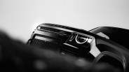 Front view of a black Land Rover Defender with a prominent grille and illuminated circular headlight, captured in a dramatic low-angle black and white photograph.