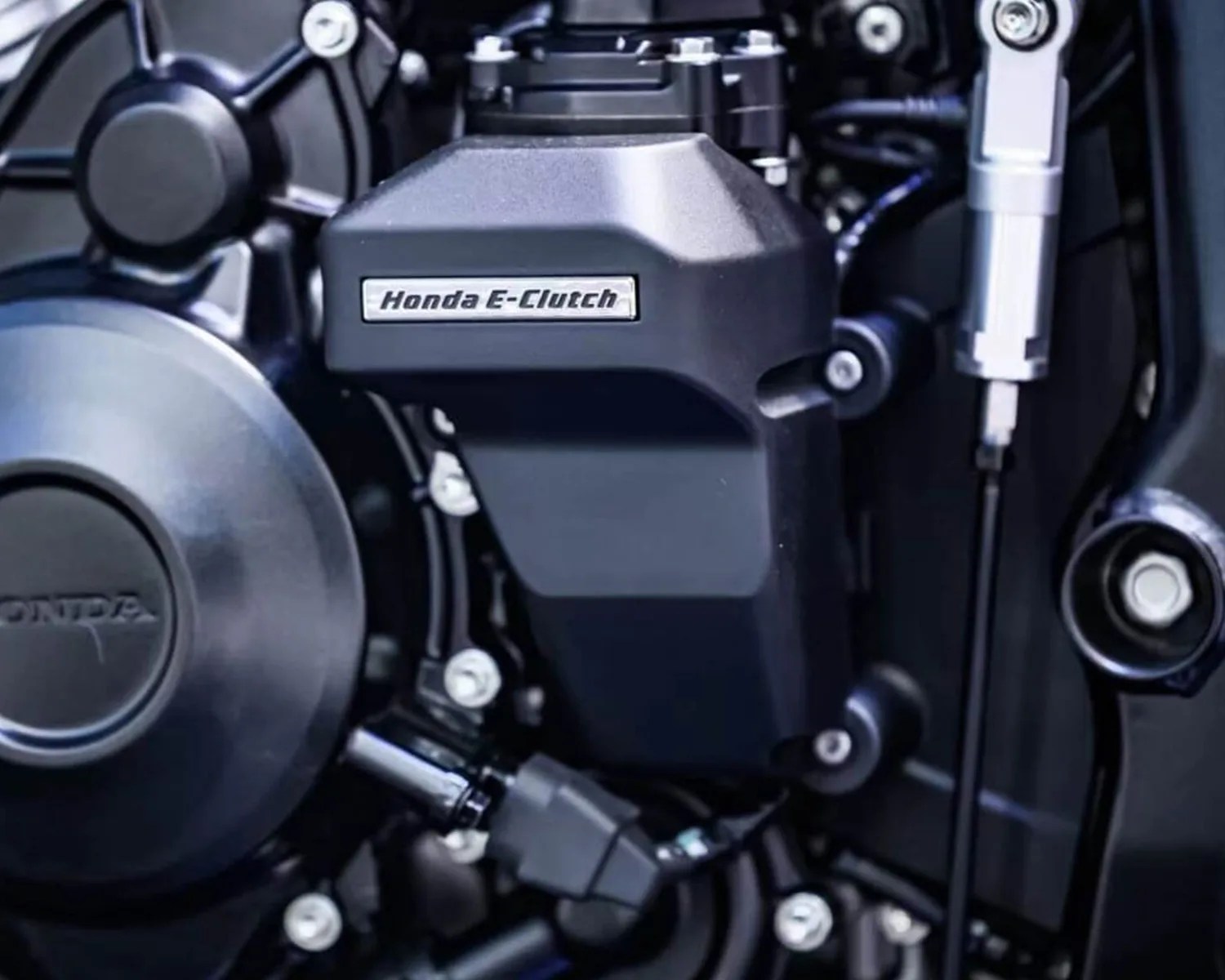 Close-up of a Honda motorcycle engine featuring a black component labeled "Honda E-Clutch," surrounded by various bolts and mechanical parts.