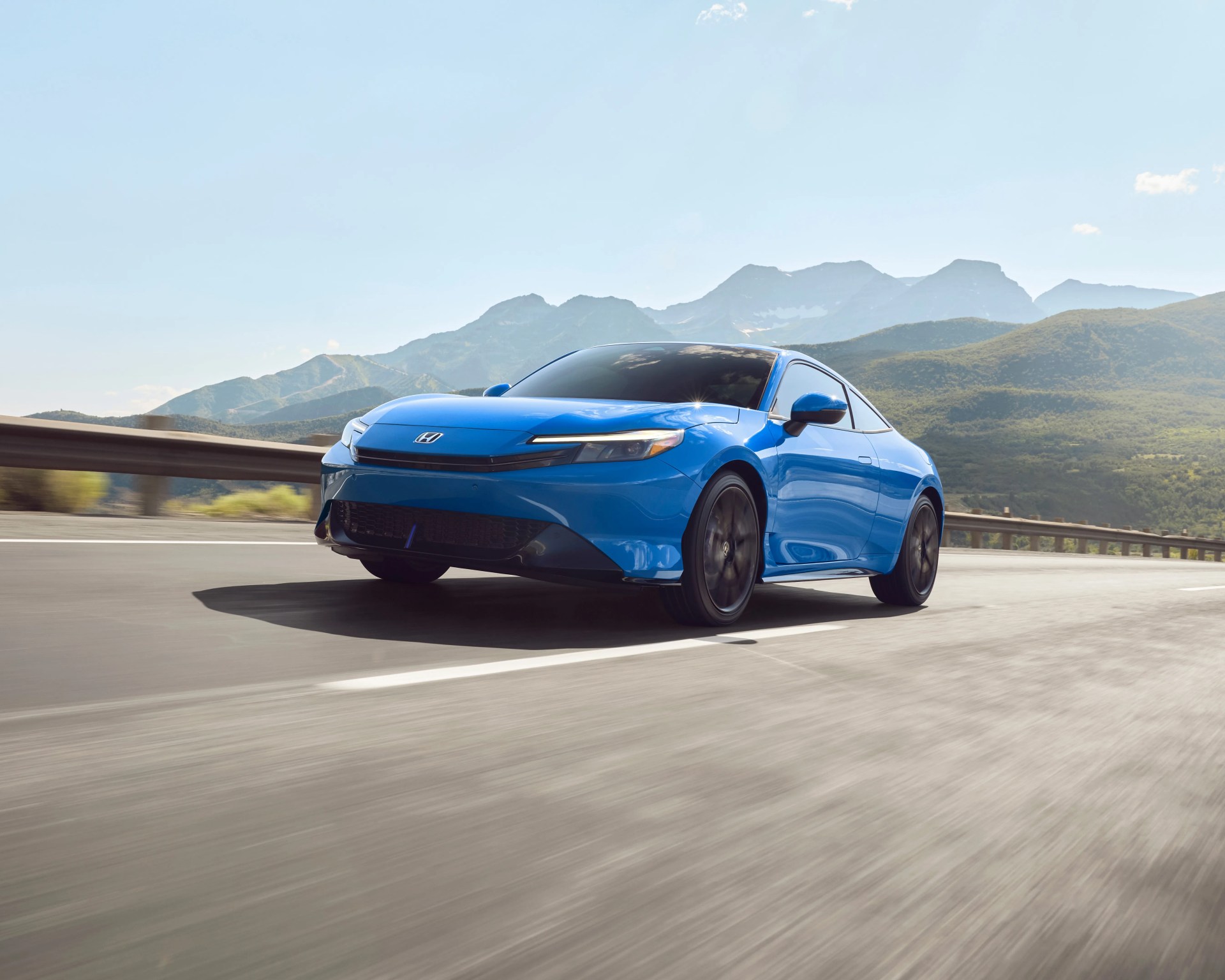 Blue Honda electric sedan driving on a highway with mountains in the background under a clear sky.
