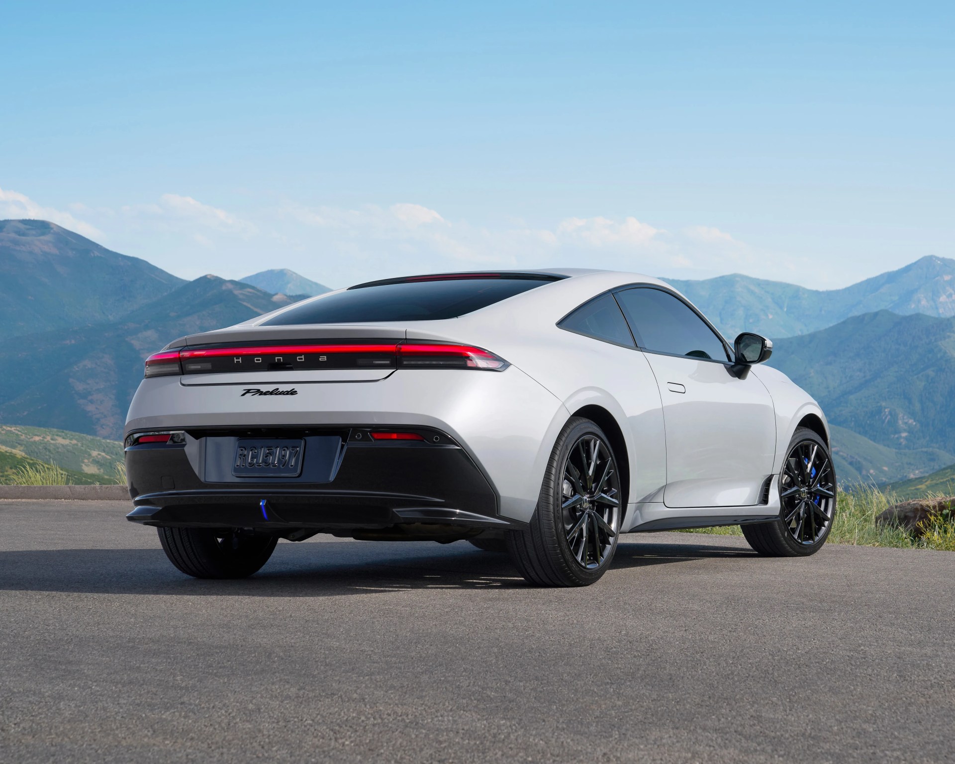 White Honda Prelude coupe with black accents, tinted windows, and black alloy wheels, parked on a paved surface with mountains and a clear blue sky in the background.