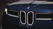 Front view of a dark blue BMW car featuring illuminated kidney grilles and sleek LED headlights with a modern, angular design. The BMW logo is centered above the grilles on the hood.