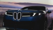 Front view of a dark blue BMW car with illuminated headlights and a distinctive kidney grille, set against a backdrop of misty hills and a soft, colorful sky.