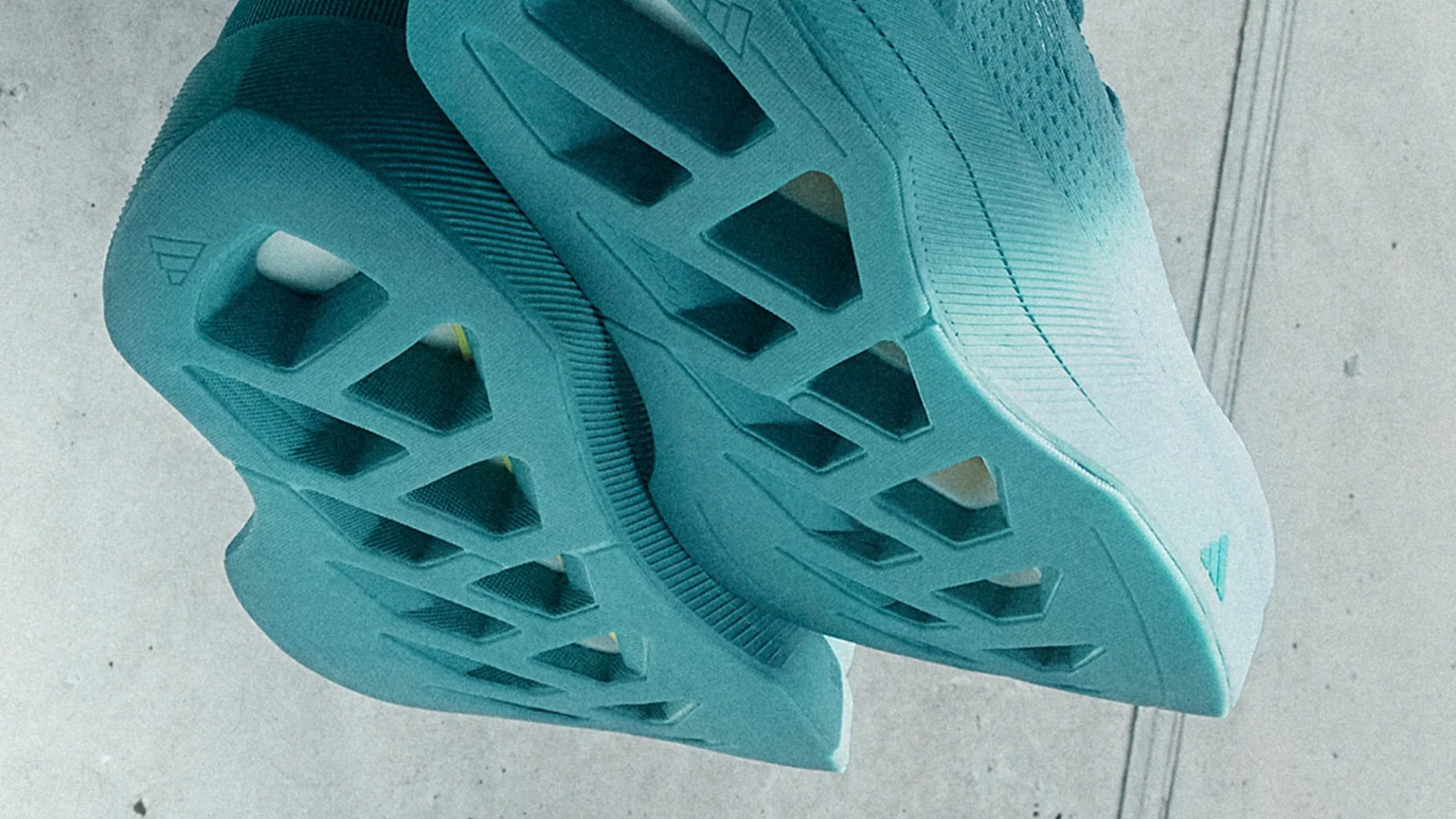 The image shows the soles of a pair of light blue athletic shoes with a unique geometric cutout design. The soles have multiple rectangular and trapezoidal openings, providing a distinctive and modern look. The shoes appear to be suspended or held up against a plain, light-colored background.