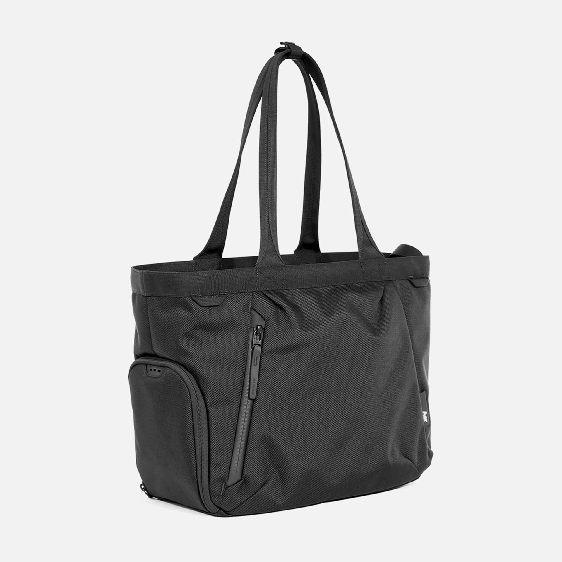 Black tote bag with two long handles, a vertical zippered pocket on the front, and an additional zippered compartment on the side. Made of durable fabric with a structured base.