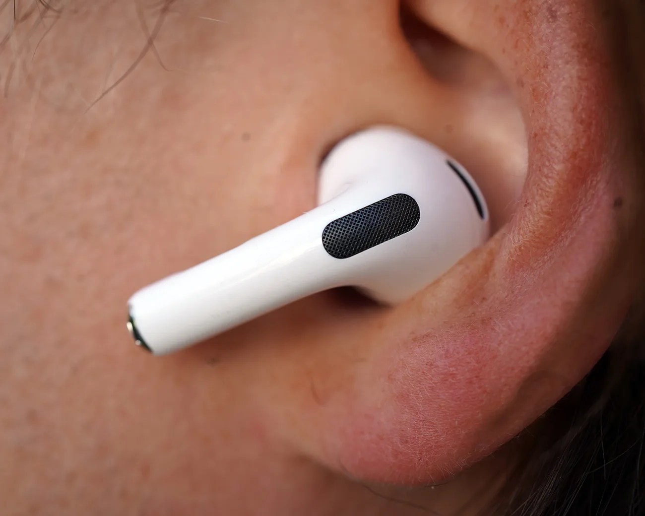 White wireless earbud inserted in a person's ear, showing the black speaker grille and smooth plastic surface.