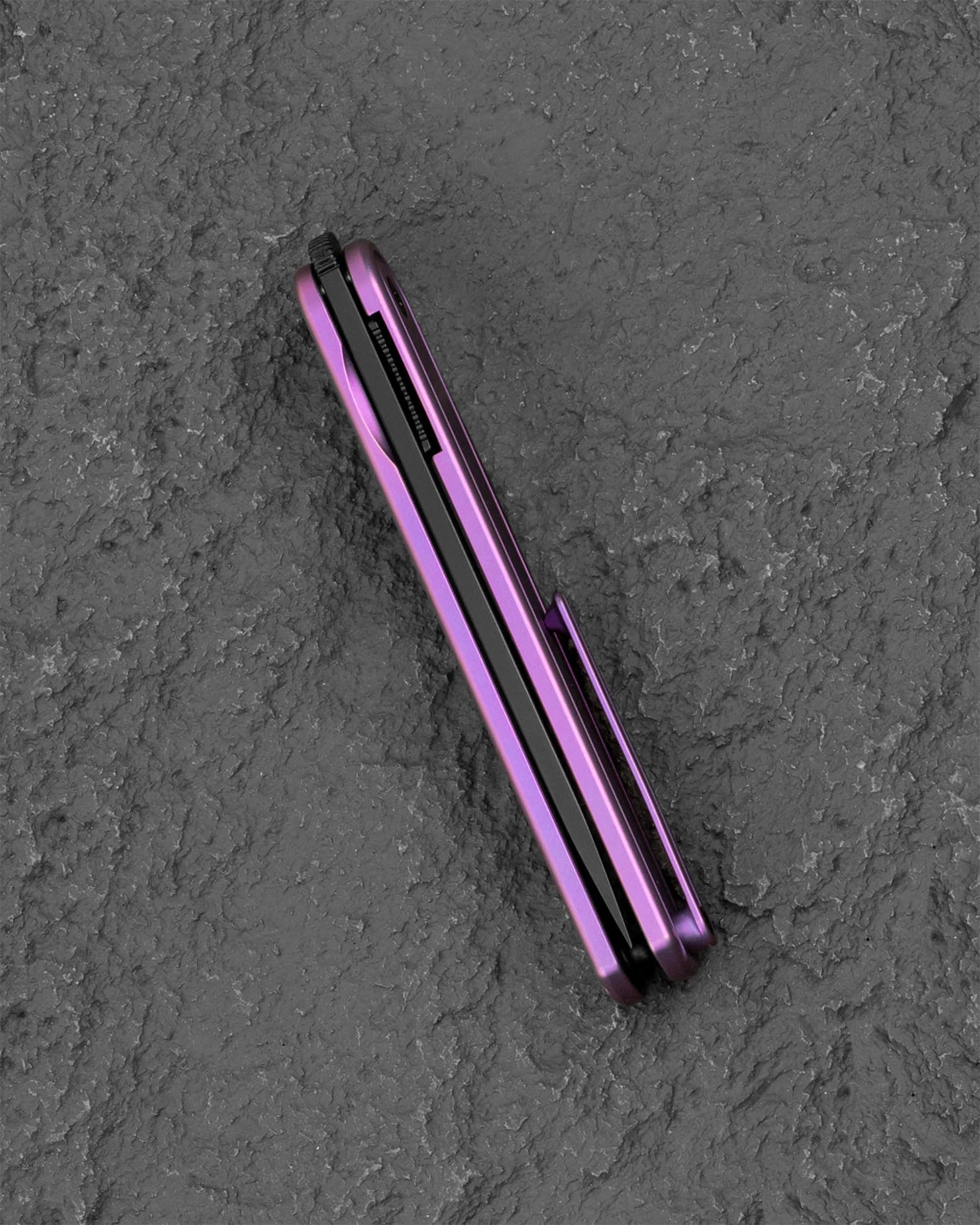 Purple folding knife with a black blade, shown closed on a textured gray surface.