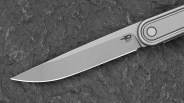 A close-up of a sleek, modern knife blade with a matte finish, featuring the "Bestech Knives" logo near the handle. The handle is metallic with a circular design element, and the knife is placed on a textured, dark surface.