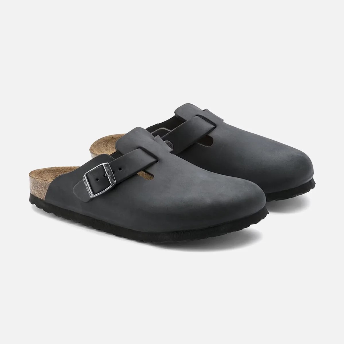 A pair of black slip-on clogs with a single adjustable strap featuring a silver buckle. The shoes have a rounded toe and a cork footbed with a black sole.