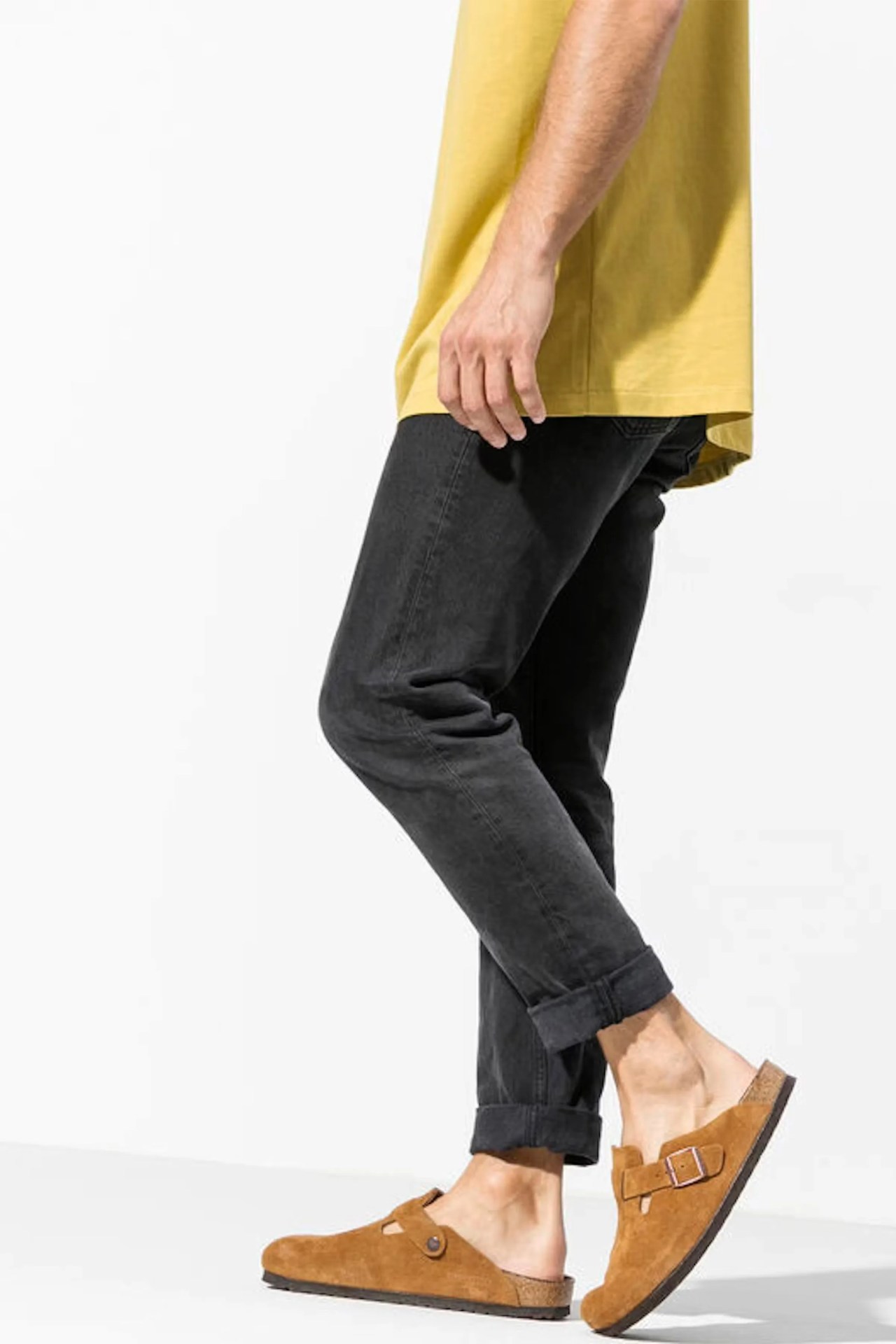 Brown suede slip-on clogs with a buckle detail, worn with black rolled-up jeans and a yellow shirt.
