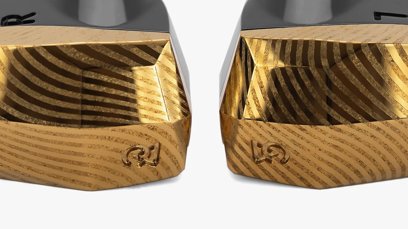 Two gold-colored, intricately patterned metallic objects with a geometric, faceted design and a small embossed logo on the front, placed side by side on a white background.
