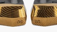 Two gold-colored, intricately patterned metallic objects with a geometric, faceted design and a small embossed logo on the front, placed side by side on a white background.