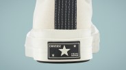 Close-up of the back heel of a white Converse sneaker with a black vertical stripe and a black rectangular label featuring the Converse logo, a large star, and the text "ATHLETIC FOOTWEAR" on the white rubber sole.