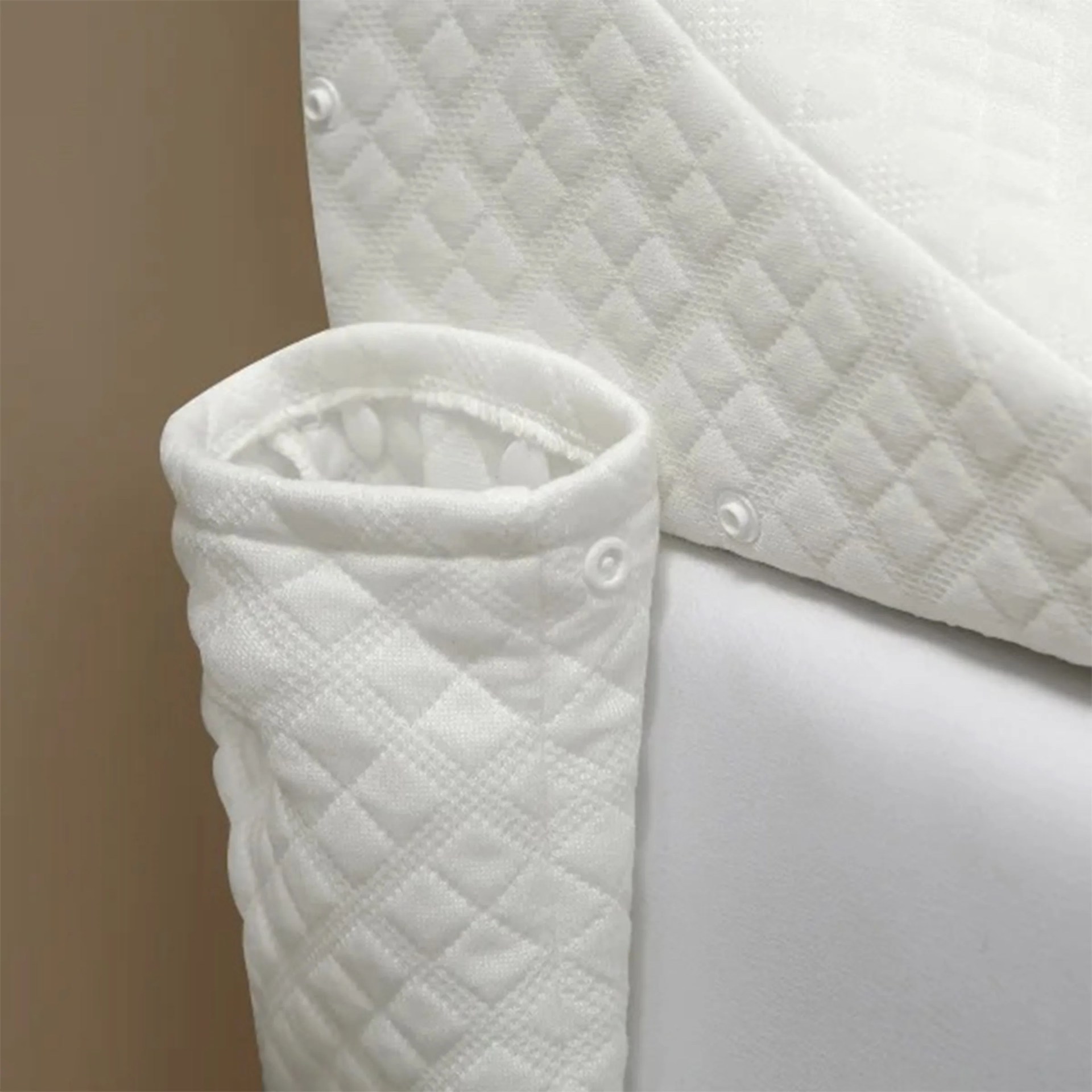 Quilted white fabric pocket attached to the side of a bed, featuring a diamond pattern and snap buttons for fastening.