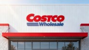Costco Wholesale store entrance with a white exterior wall, red and blue logo, and a red awning above glass doors.