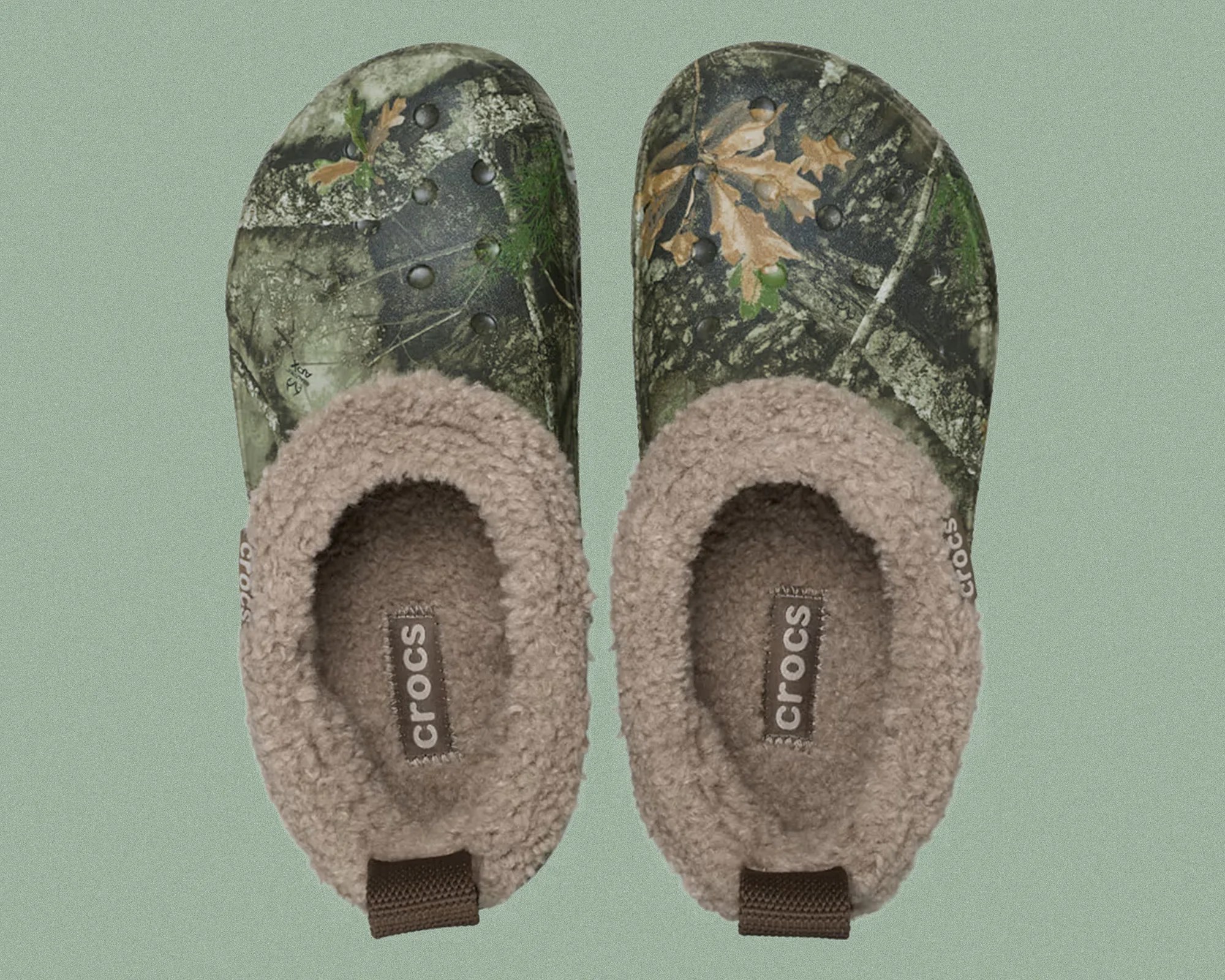 Pair of Crocs clogs with a camouflage pattern on the exterior and a soft, fuzzy brown lining on the interior. The Crocs logo is visible on the insole and the side of each clog.