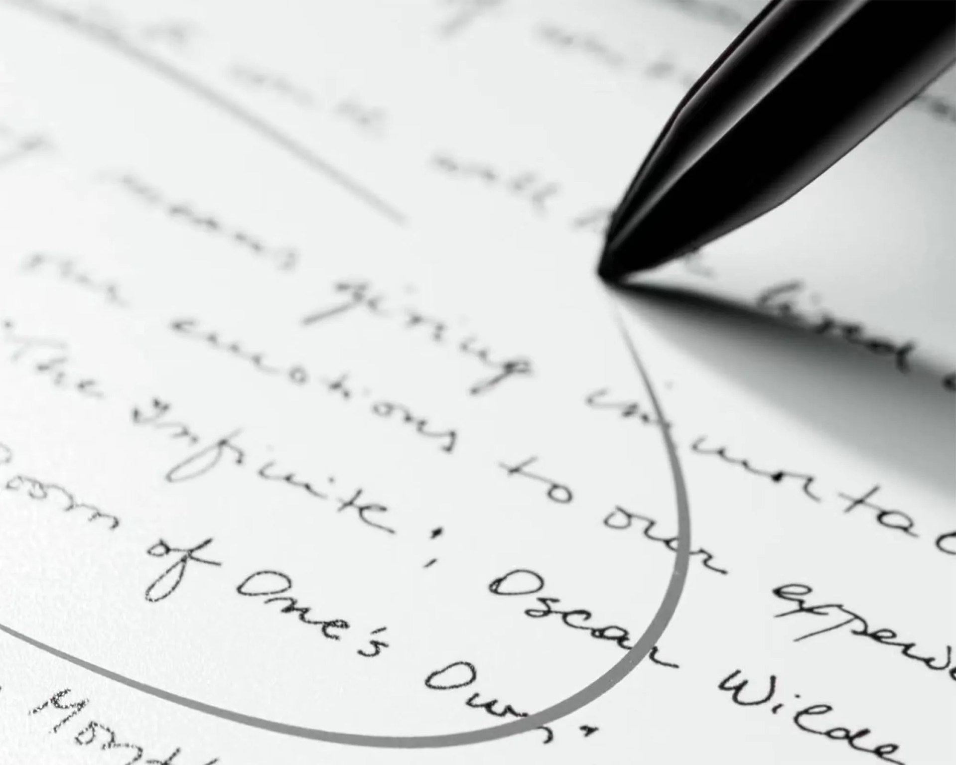 Close-up of a black pen writing on a white sheet of paper with cursive handwriting, including a quote attributed to Oscar Wilde. The pen's tip is touching the paper, and a curved line is drawn around part of the text.