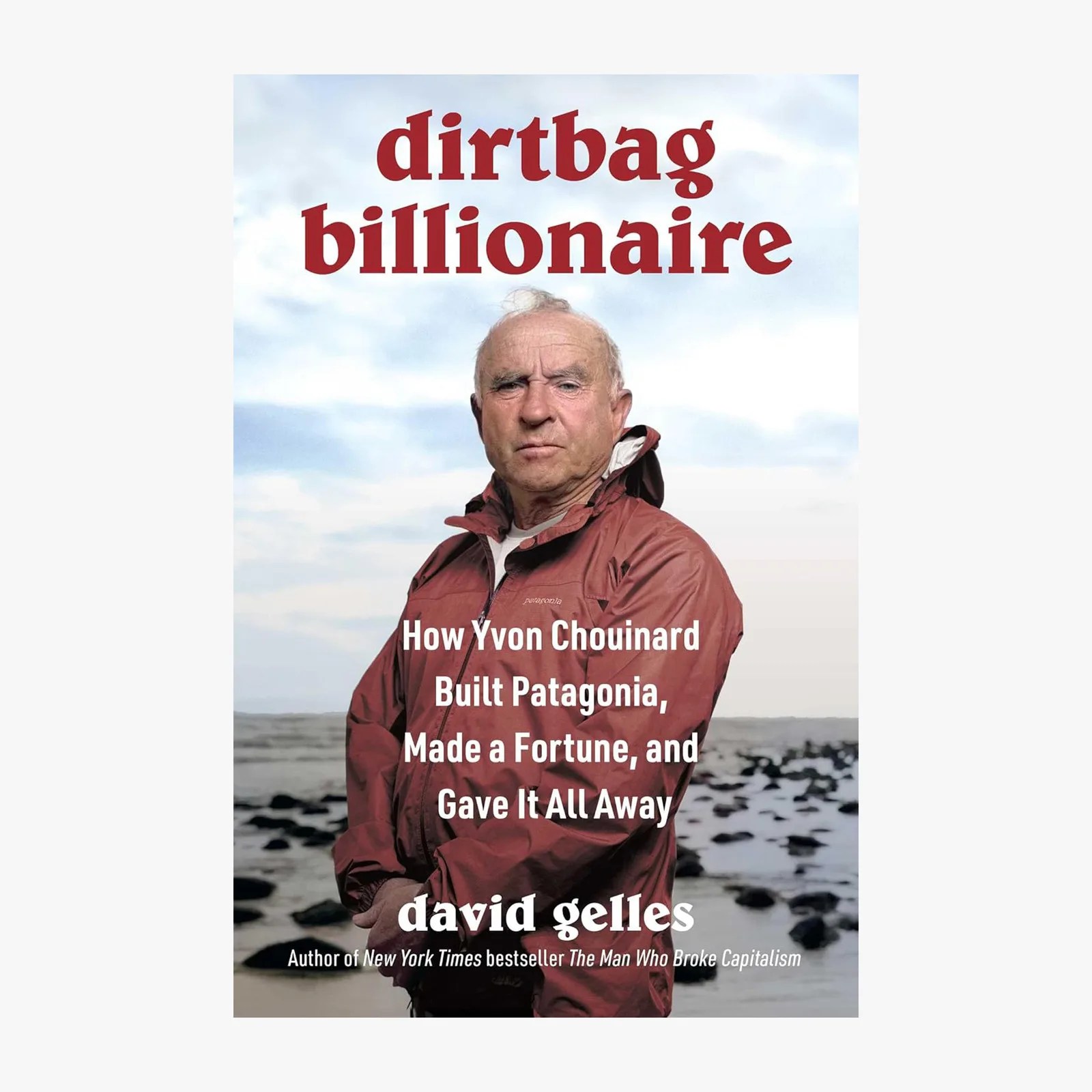 Dirtbag Billionaire book cover featuring a man in a red Patagonia jacket standing with arms crossed against a rocky shoreline background. The title "dirtbag billionaire" is in large red text at the top. Below the man, white text reads: "How Yvon Chouinard Built Patagonia, Made a Fortune, and Gave It All Away." The author's name, "david gelles," is at the bottom with a note that he is the author of the New York Times bestseller The Man Who Broke Capitalism.