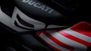 Close-up of a Ducati motorcycle fuel tank and side panel, featuring a matte black finish with white and red graphic accents and the "DUCATI" logo in bold letters. The side panel has a red and white striped design.