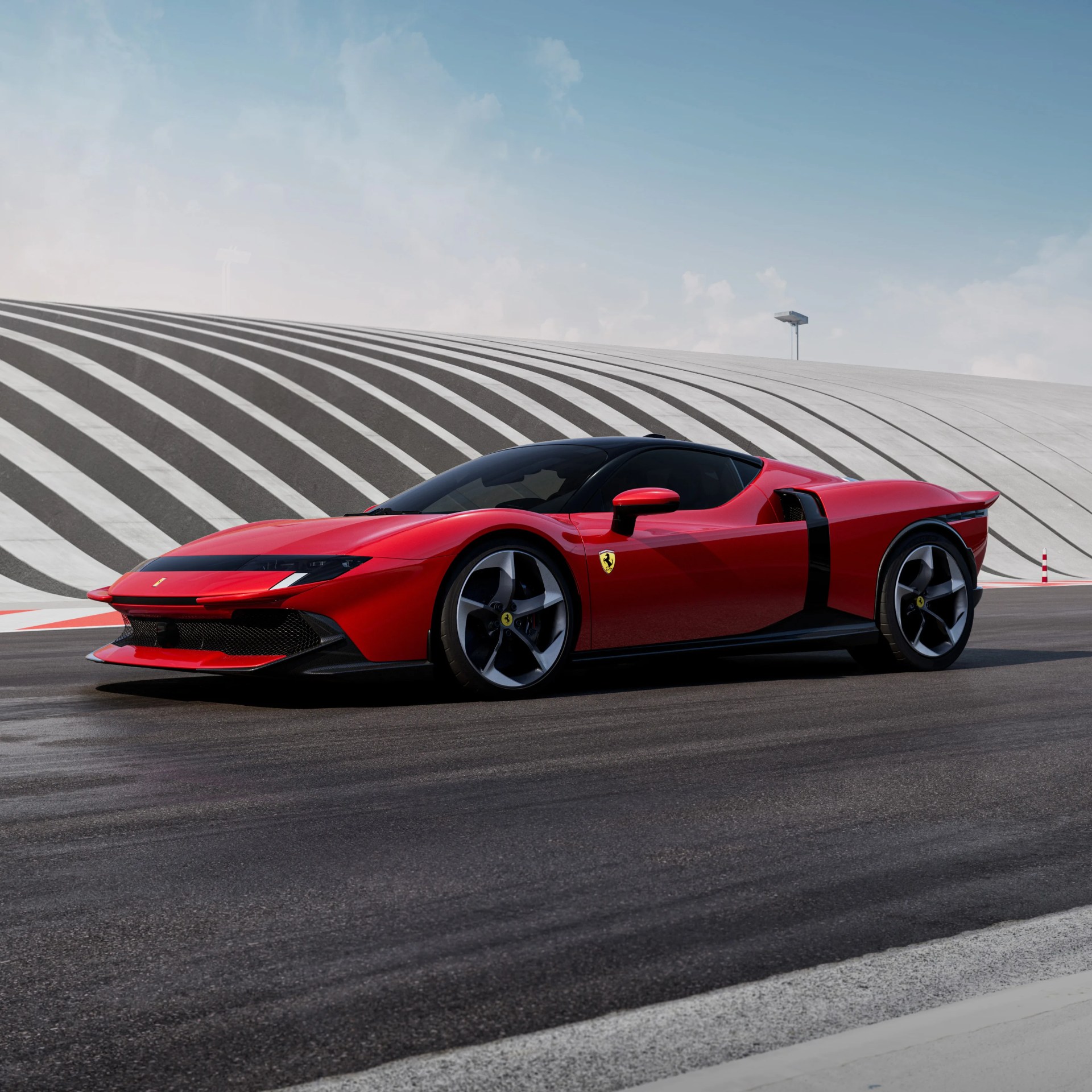Red Ferrari sports car with black roof and aerodynamic design, parked on a racetrack with a striped, curved concrete wall in the background.